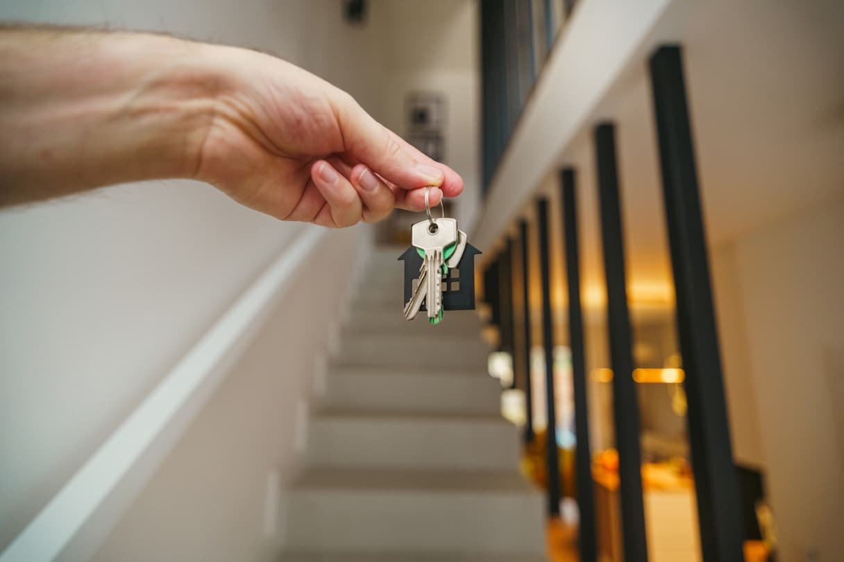 A hand holding house keys on a staircase